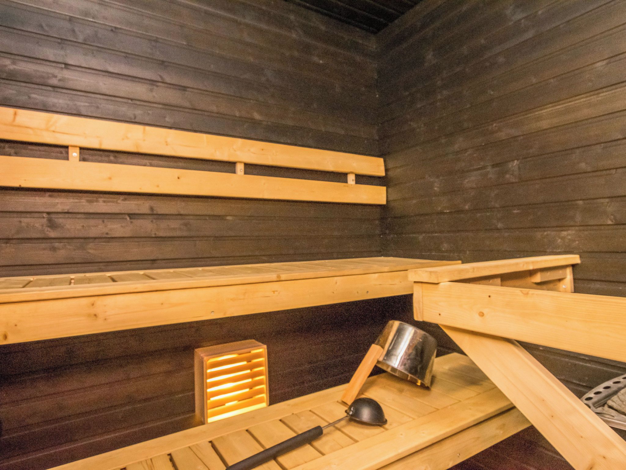 Een sauna met houten banken en een metalen emmer.