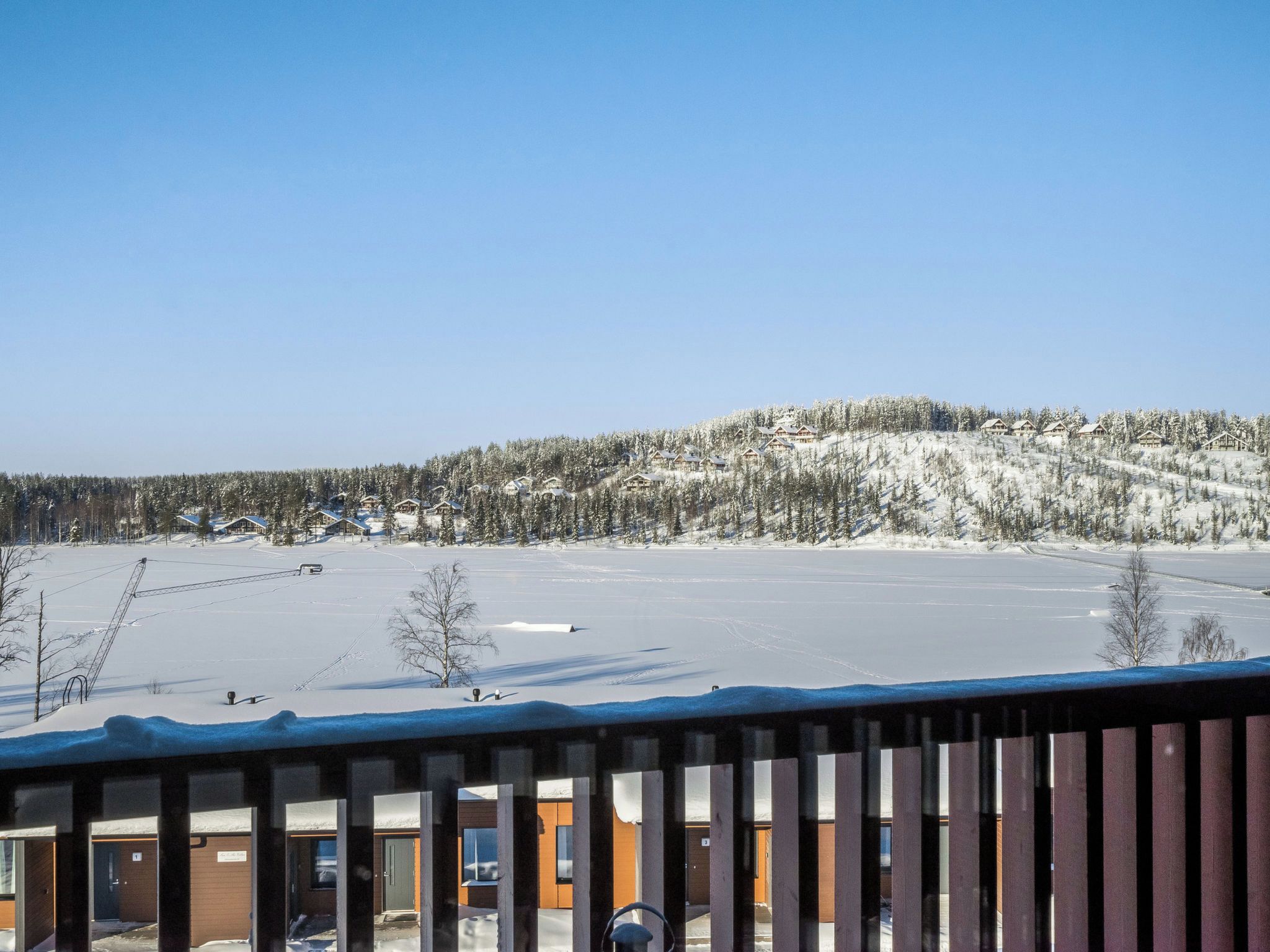 A snowy landscape with a clear sky, a wooden cabin, and a snow-covered hill.