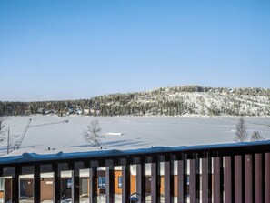 A snowy landscape with a clear sky, a wooden cabin, and a snow-covered hill.