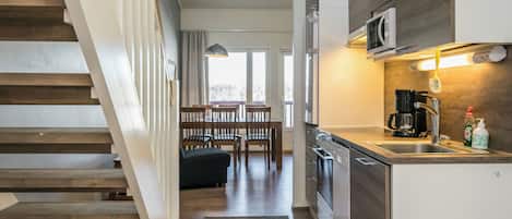 A modern kitchen with a built-in microwave, coffee maker, and dishwasher. A wooden staircase leads to a dining area with a view of the outdoors.