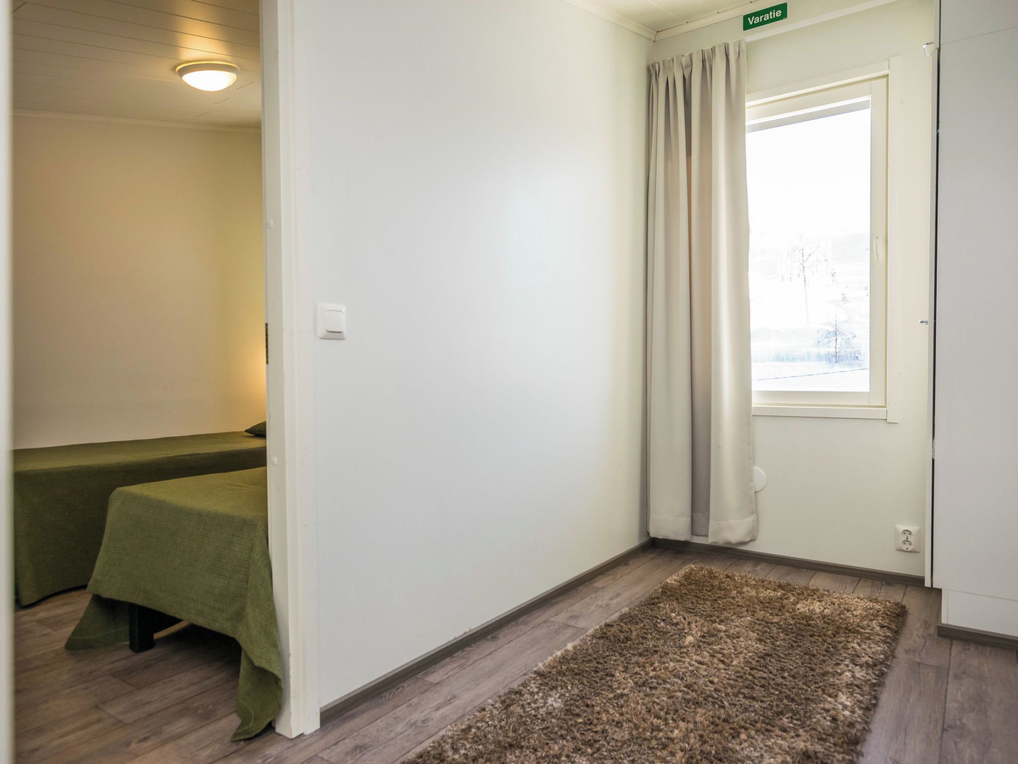 A hotel room with a bed, a small table, a window with curtains, and a carpeted floor.
