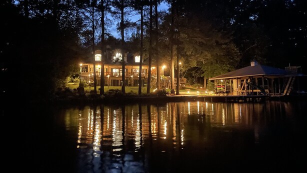 A large, illuminated lakeside lodge with multiple levels and a dock extending into the water. - GREAT for FAMILIES, beautiful waterfront, kayaks, firepit, pool table, & more! (Henrico)