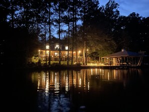 A large, illuminated lakeside lodge with multiple levels and a dock extending into the water. - GREAT for FAMILIES, beautiful waterfront, kayaks, firepit, pool table, & more! (Henrico)