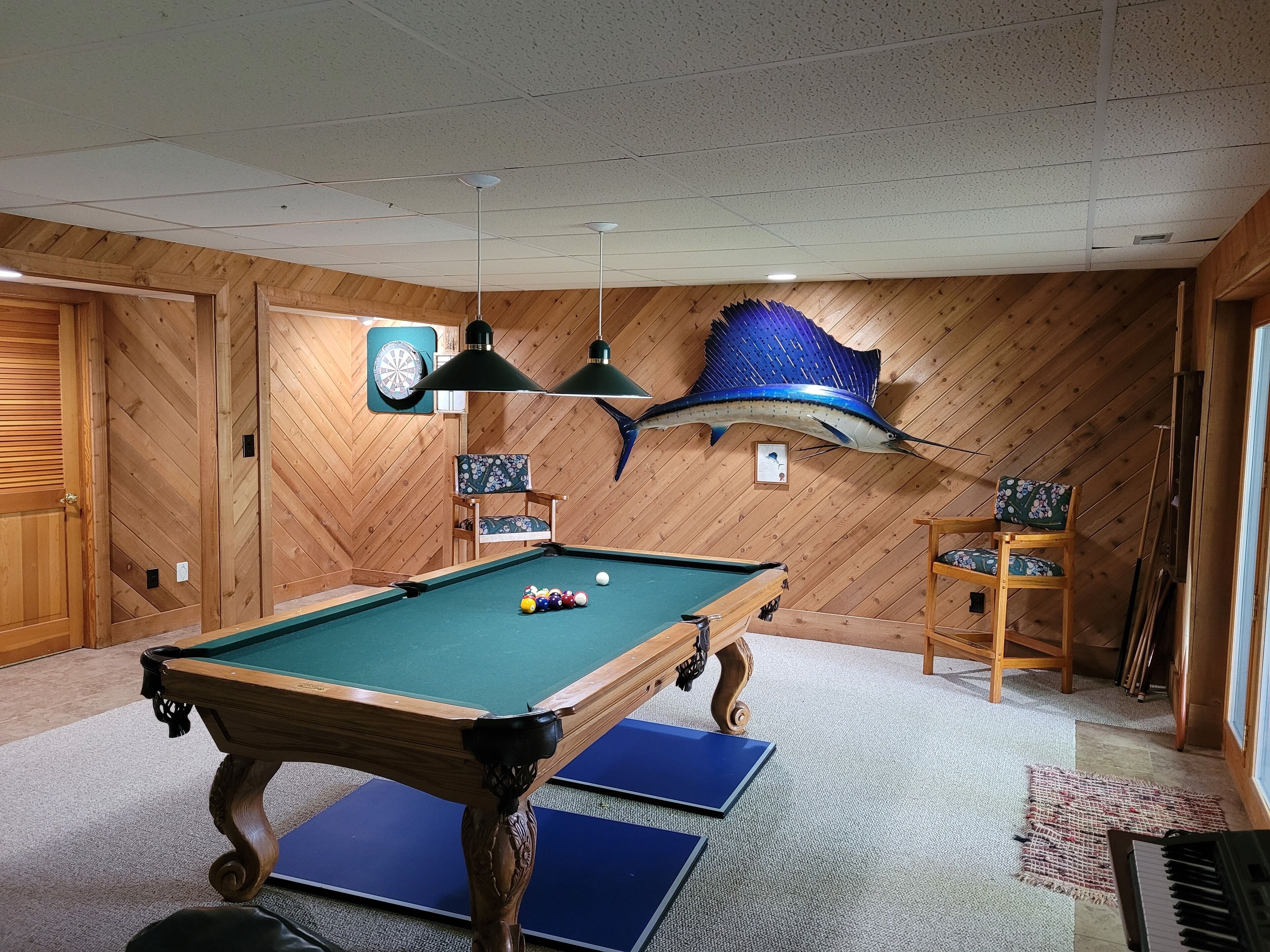 A pool table with billiard balls, a dartboard, and a large fish decoration on the wall.