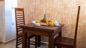 A wooden dining table with breakfast items, two wooden chairs, and a brick wall background. - Gardenia Eco Apartment in Panormo (Panormos)