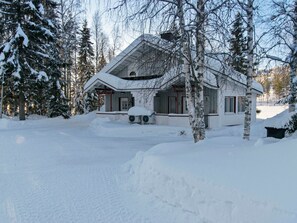 Een huis bedekt met sneeuw met een grote garage, omringd door bomen en een besneeerd landschap.
