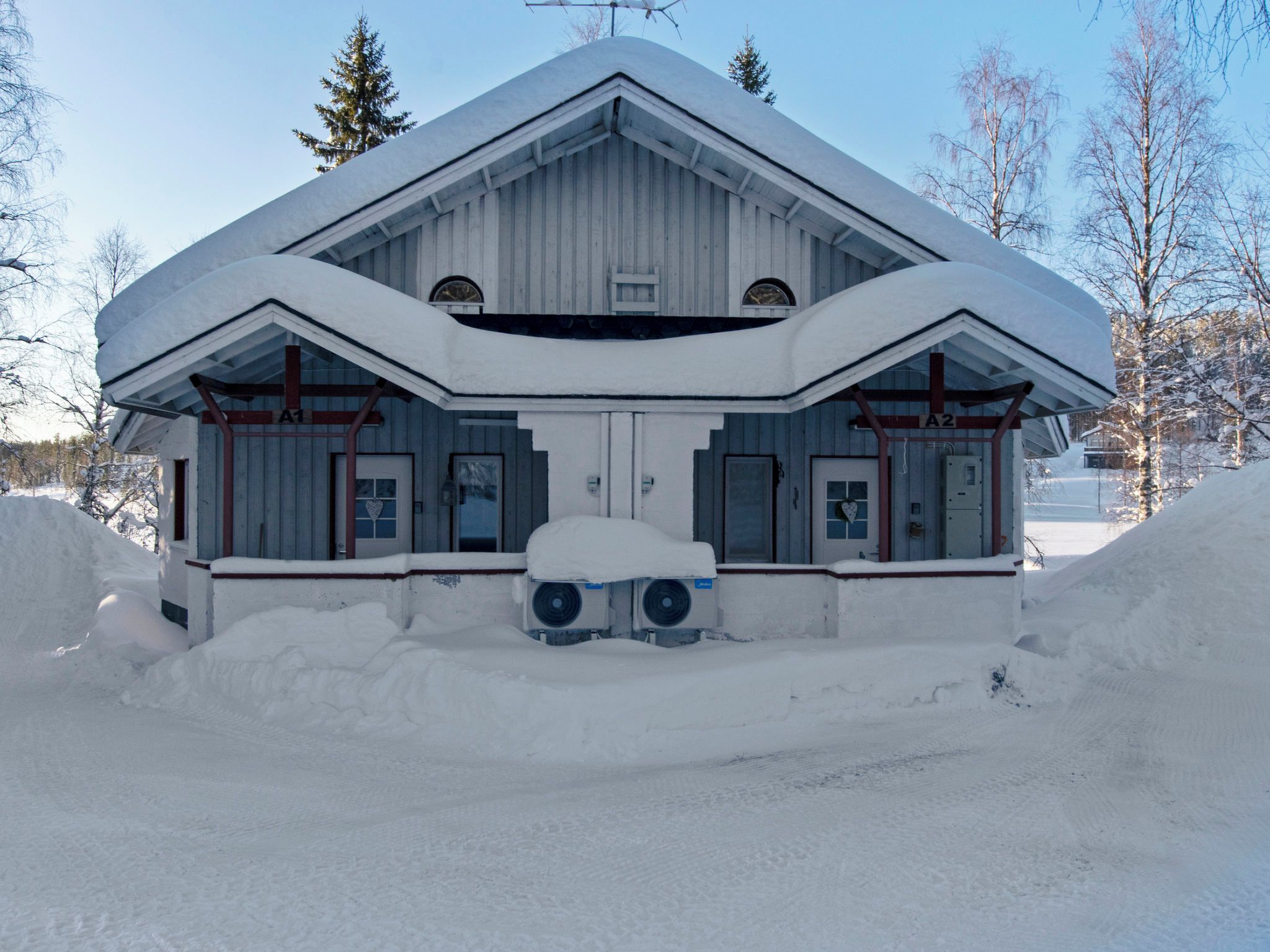 Un edificio cubierto de nieve con una fachada simétrica, dos unidades de aire acondicionado grandes al frente y un cielo despejado.