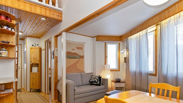 A cozy room with a sofa, a dining table with chairs, a bookshelf, and a window with curtains. - Hallantytär a2 paritalo by Interhome (Hyrynsalmi)