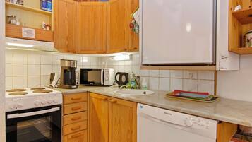 Cozinha compacta com armários de madeira, geladeira branca, micro-ondas, cafeteira e lava-louças.