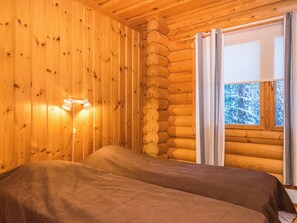 Een blokhutkamer met een bed, een wandlamp en een raam met gordijnen.