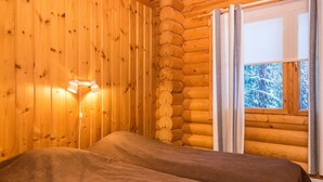 Et hytteværelse med seng, væglampe og et vindue med gardiner.
