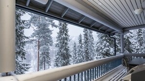 En balkon med gelænder i metal, der kigger ud over en sneklædt skov.