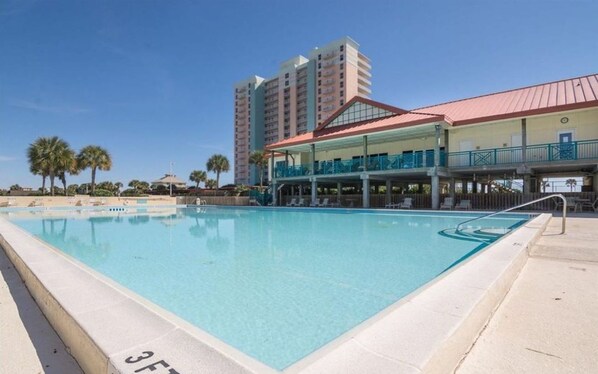 A swimming pool with a clear blue water, surrounded by a building with a red roof and a balcony. - ROOMY 3 bedroom Waterview Sleeps 9-Pool Balcony Dock Pickleball on Trolley Stop (Pensacola Beach)