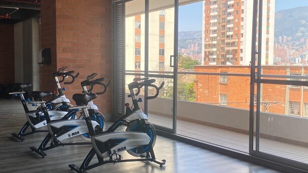 A gym with stationary bikes, large windows, and a view of buildings.