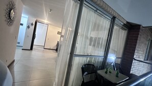 A room with a dining area, a window with curtains, a chair, and a table with bottles.