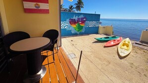Um pátio com mesa, cadeiras, um mural e caiaques à beira-mar.