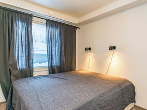 Une chambre à coucher avec un lit, des rideaux, une fenêtre avec des stores et deux lampes fixées au mur.