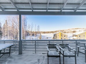 A covered outdoor seating area with metal railings and benches, snow-covered ground, and a view of houses and trees in the background.