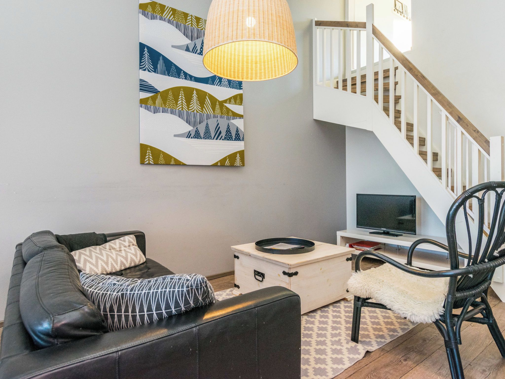 Een moderne woonkamer met een bank, een televisie, een decoratieve lamp en een trap.