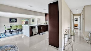 Una cocina moderna con una isla central, zona de comedor con sillas y un pasillo que conduce a otra habitación.