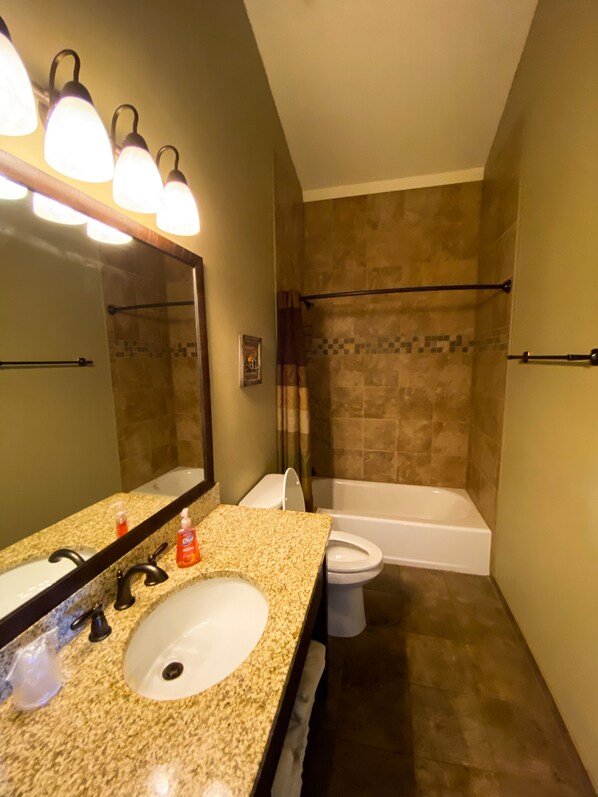 A bathroom with a granite countertop sink, a mirror, a toilet, and a bathtub.