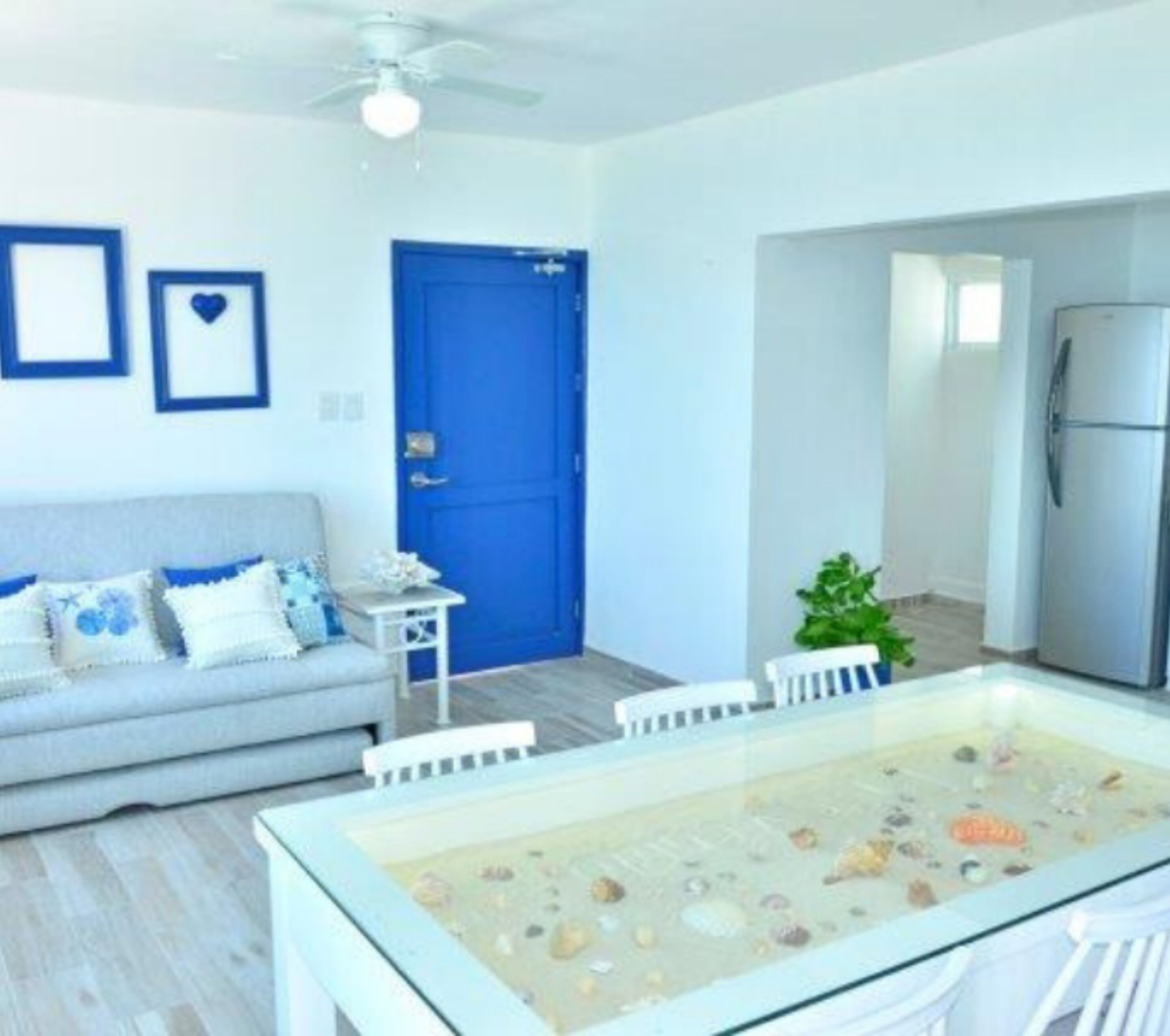 A modern living room with a sofa, a dining table with a glass top, a blue door, and a refrigerator.