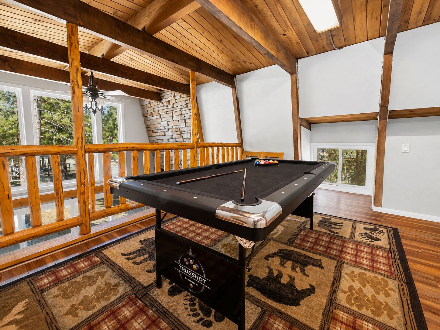A pool table in a room with wooden beams, a stone wall, and a view through large windows. - Sherwood Pines - Pool Table, Fireplace, Fenced Yard (Big Bear City)