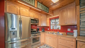 A kitchen with wooden cabinets, stainless steel appliances, a water dispenser, and a patterned rug. - Sherwood Pines - Pool Table, Fireplace, Fenced Yard (Big Bear City)