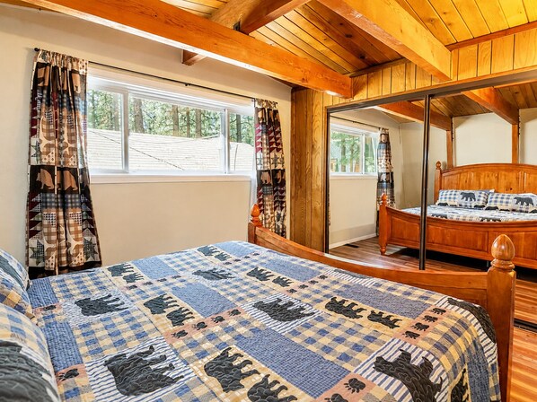 A bedroom with a large bed, a wooden headboard, a mirror, and a window with curtains. - Sherwood Pines - Pool Table, Fireplace, Fenced Yard (Big Bear City)
