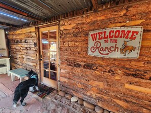 Une façade rustique en bois, agrémentée d’une enseigne « Bienvenue au ranch », d’une porte vitrée et d’un banc à l’extérieur.