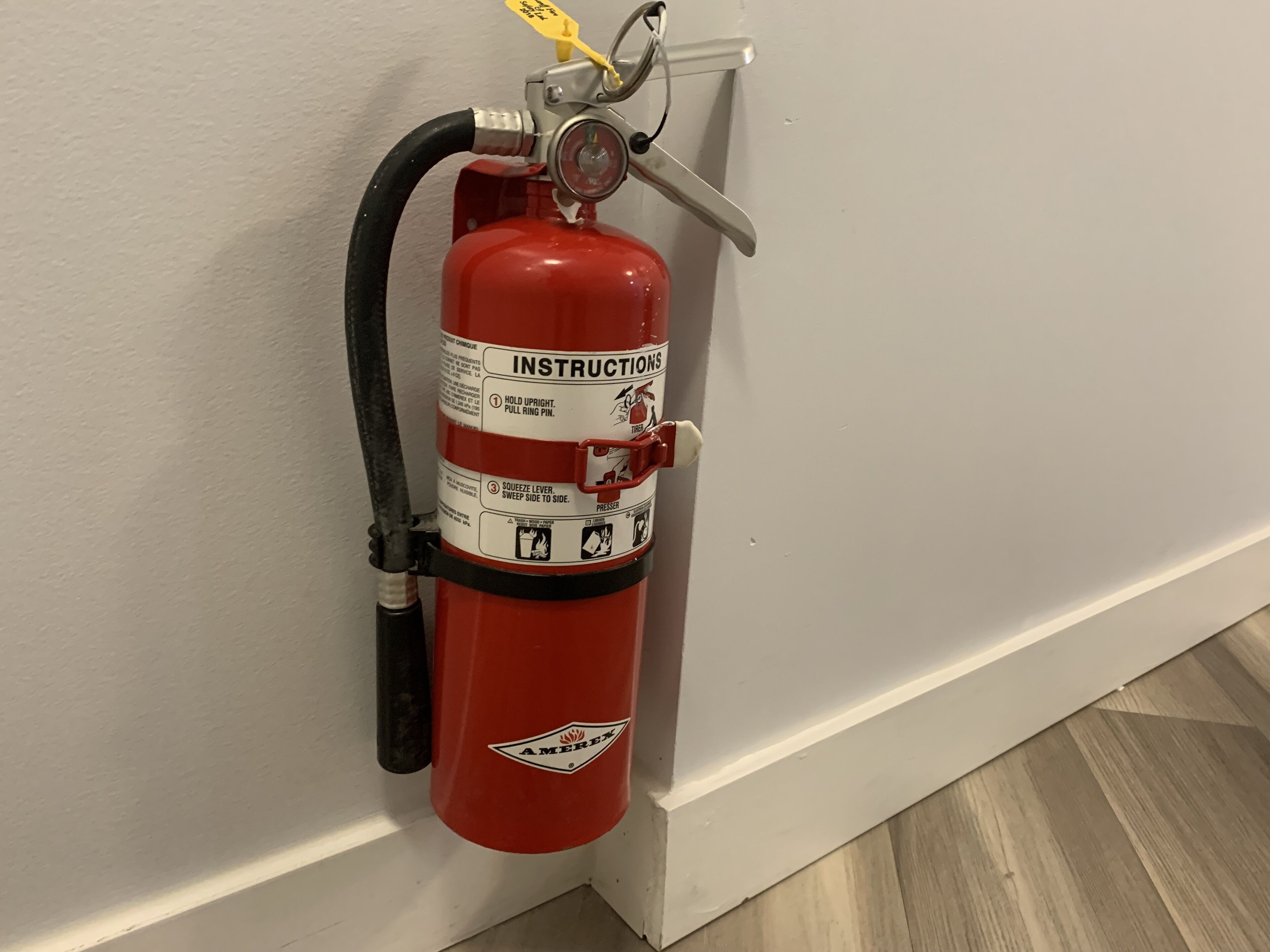 Een rode brandblusser bevestigd aan een witte muur in de buurt van een houten vloer.
