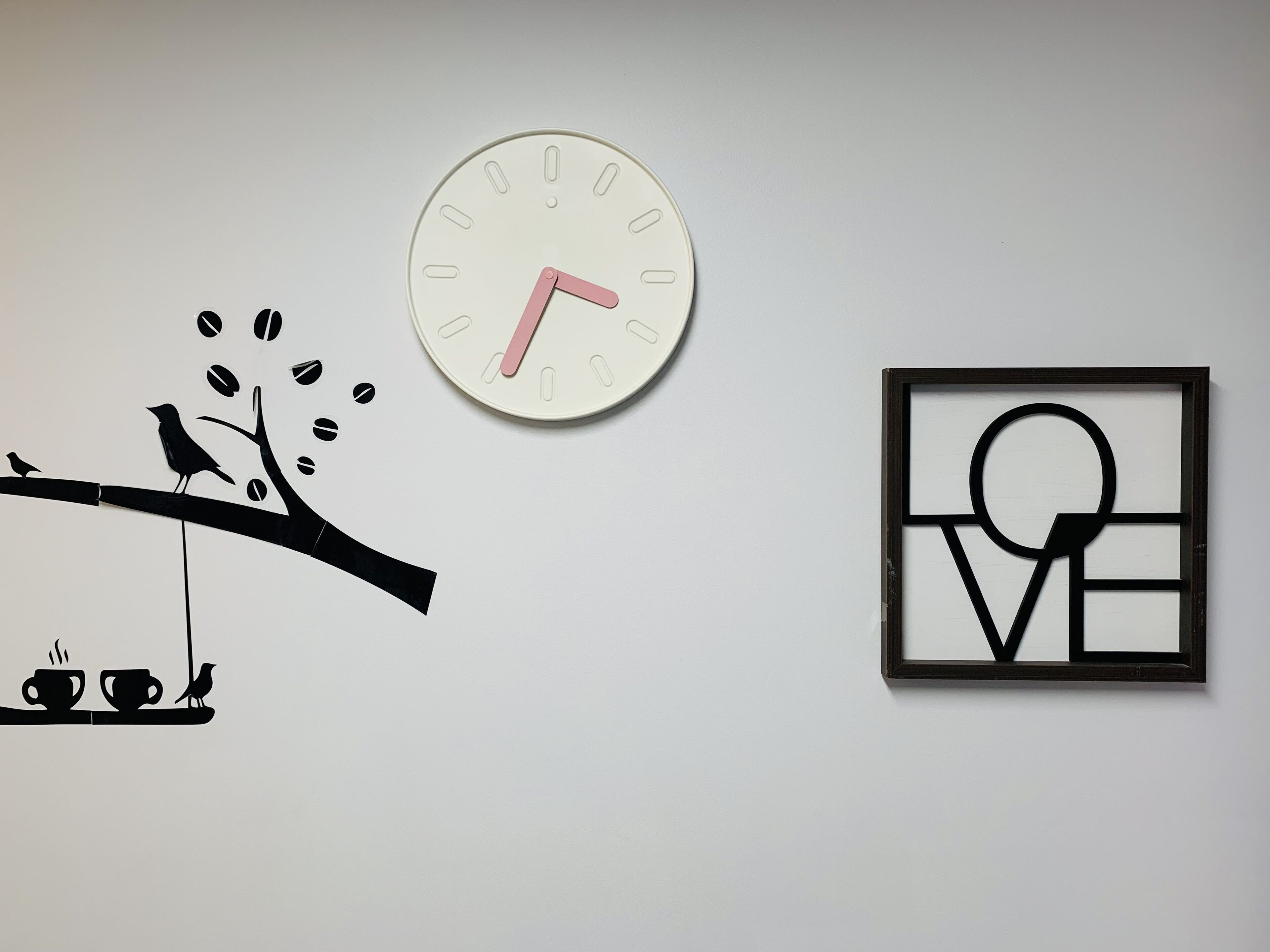 Una pared con un reloj, la silueta de un pájaro sobre una rama y un cuadro abstracto enmarco.