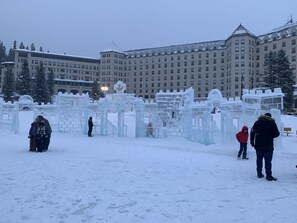 Zona exterior cubierta de nieve con esculturas de hielo y un edificio grande al fondo.