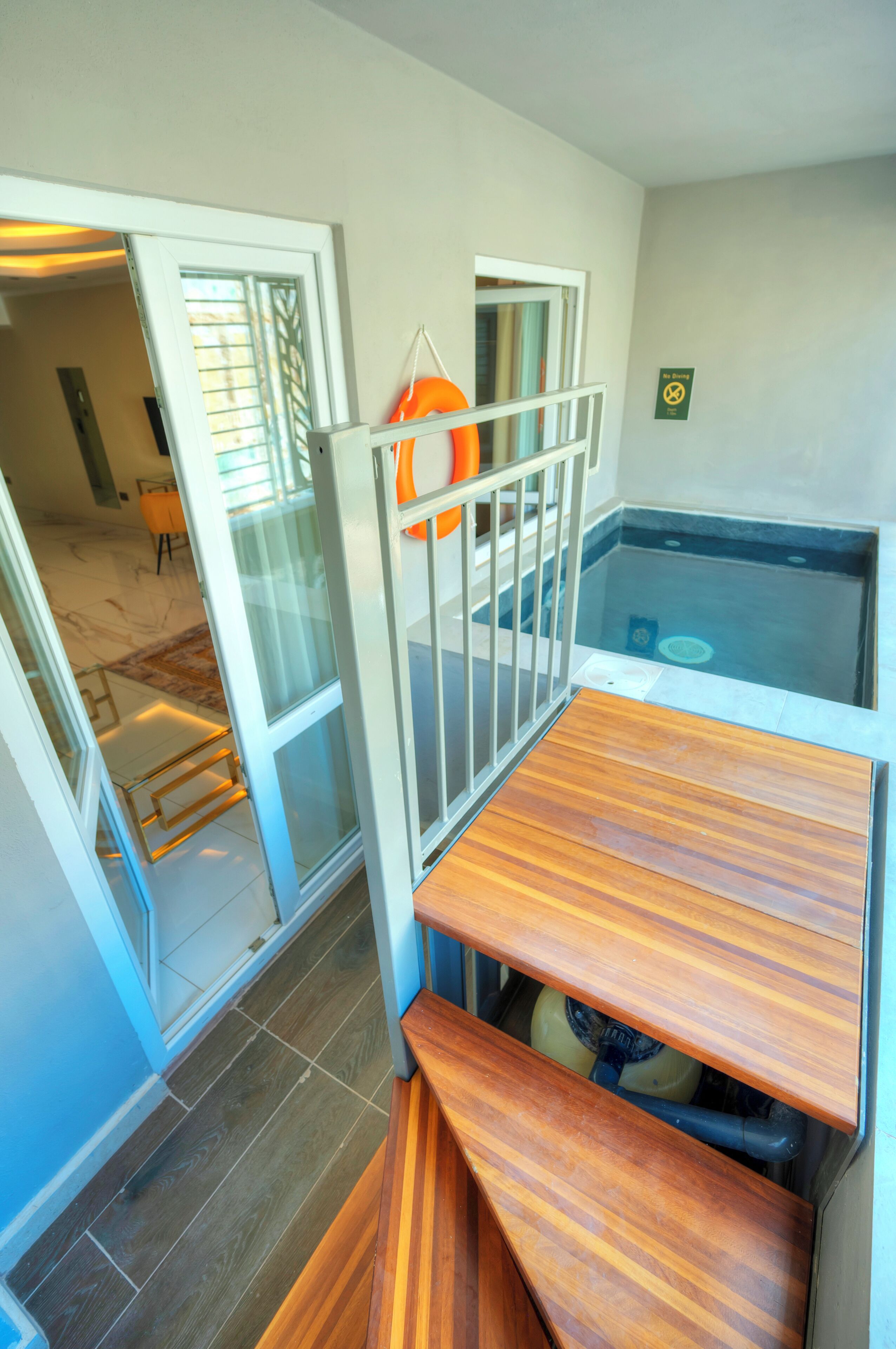 Une pièce avec un banc en bois, une porte vitrée donnant sur une autre pièce et un petit espace piscine équipé d’une bouée de sauvetage.