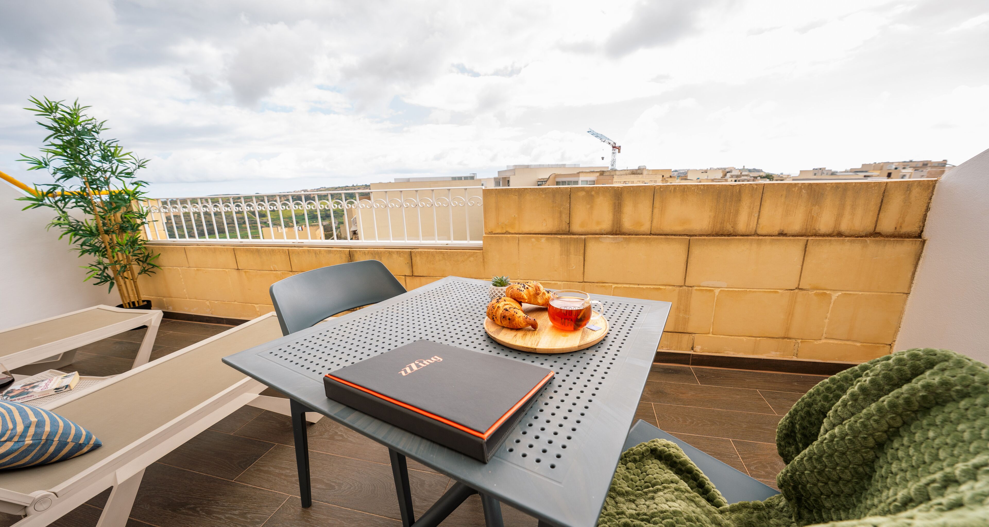 A balcony with a table, chairs, a plant, and a view of the cityscape.