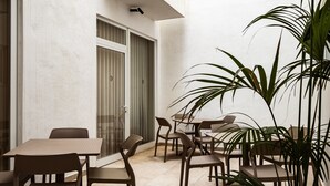 Een terras buiten met meerdere tafels en stoelen, een schuifpui en potplanten.