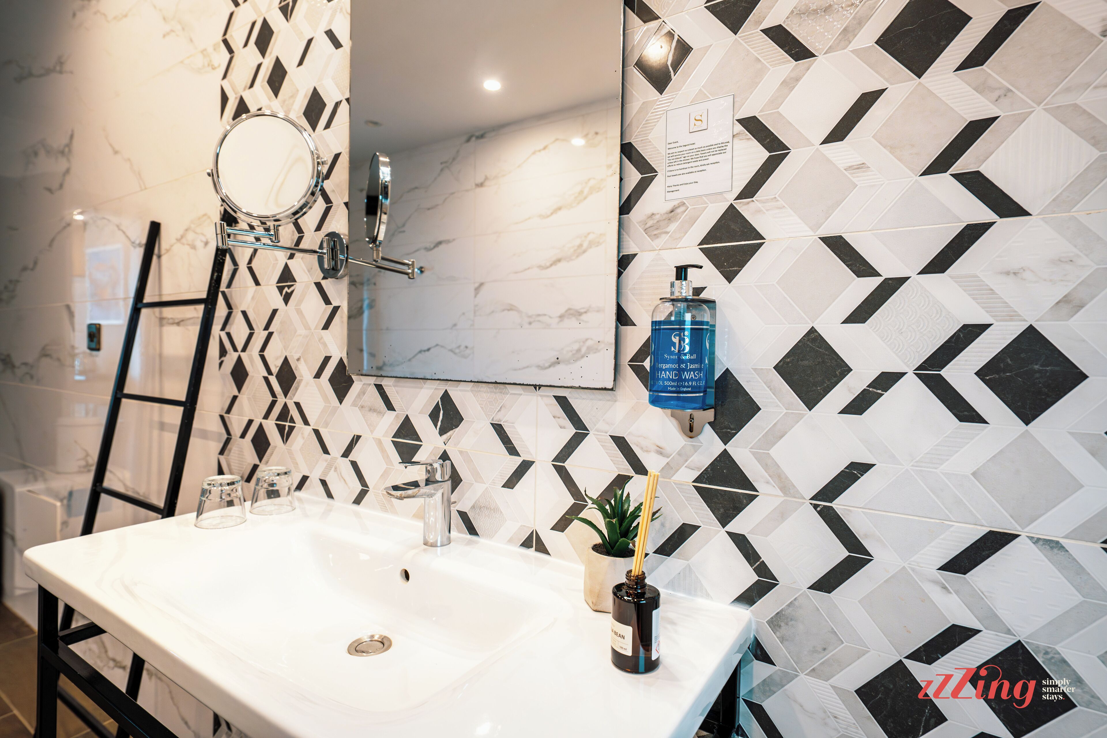 A bathroom with a white sink, a mirror, a towel rack, and a geometric-patterned wall.
