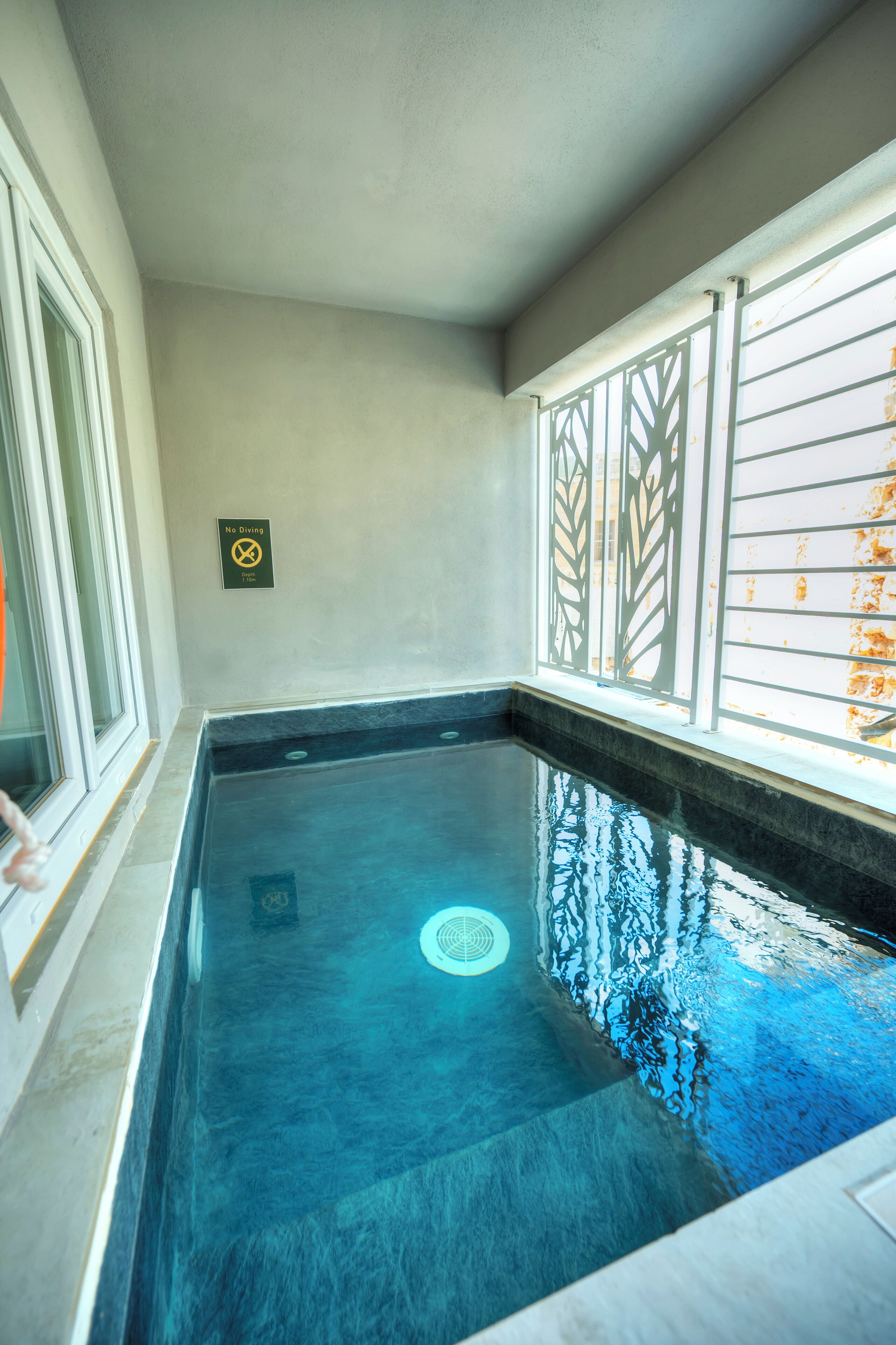 A swimming pool with a 'No Diving' sign, a window with a leaf pattern, and a 'No Diving' sign on the wall.