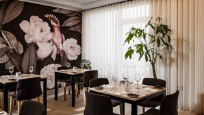 Een eetruimte met gedekte tafels, een grote bloemenmuur en een grote plant bij het raam.