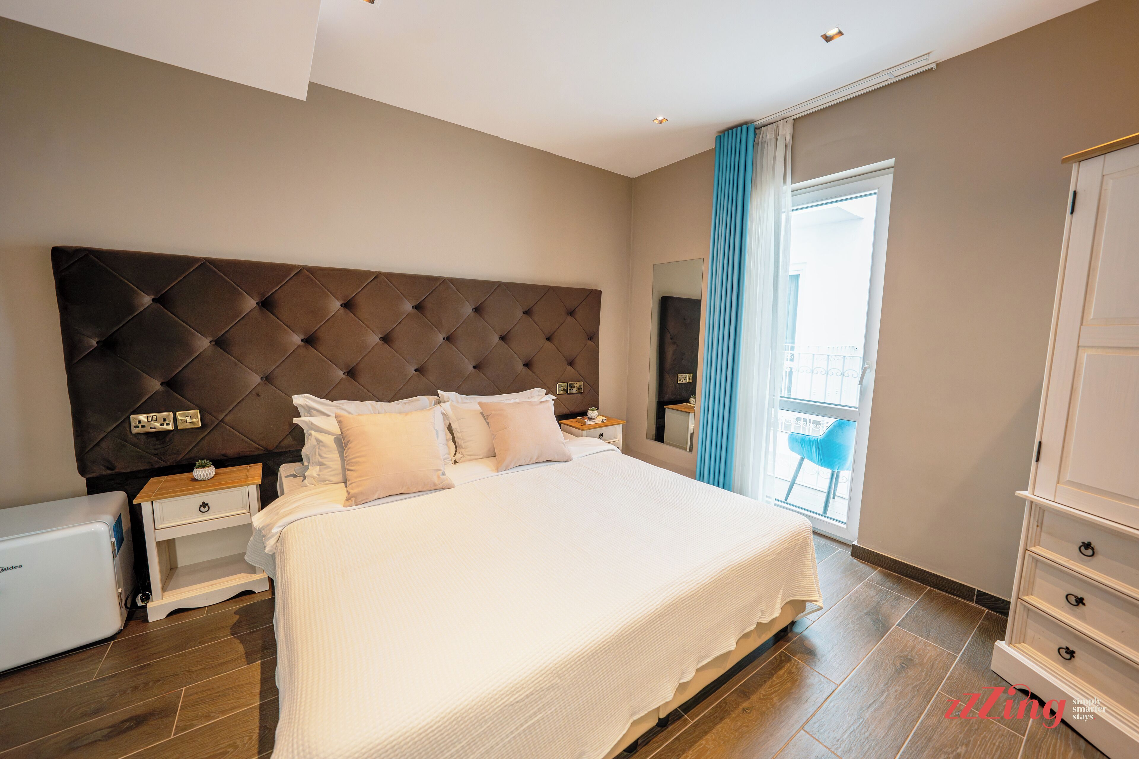 Una habitación de hotel moderna con una cama grande, una mesita de noche, un aparador y vistas al exterior.