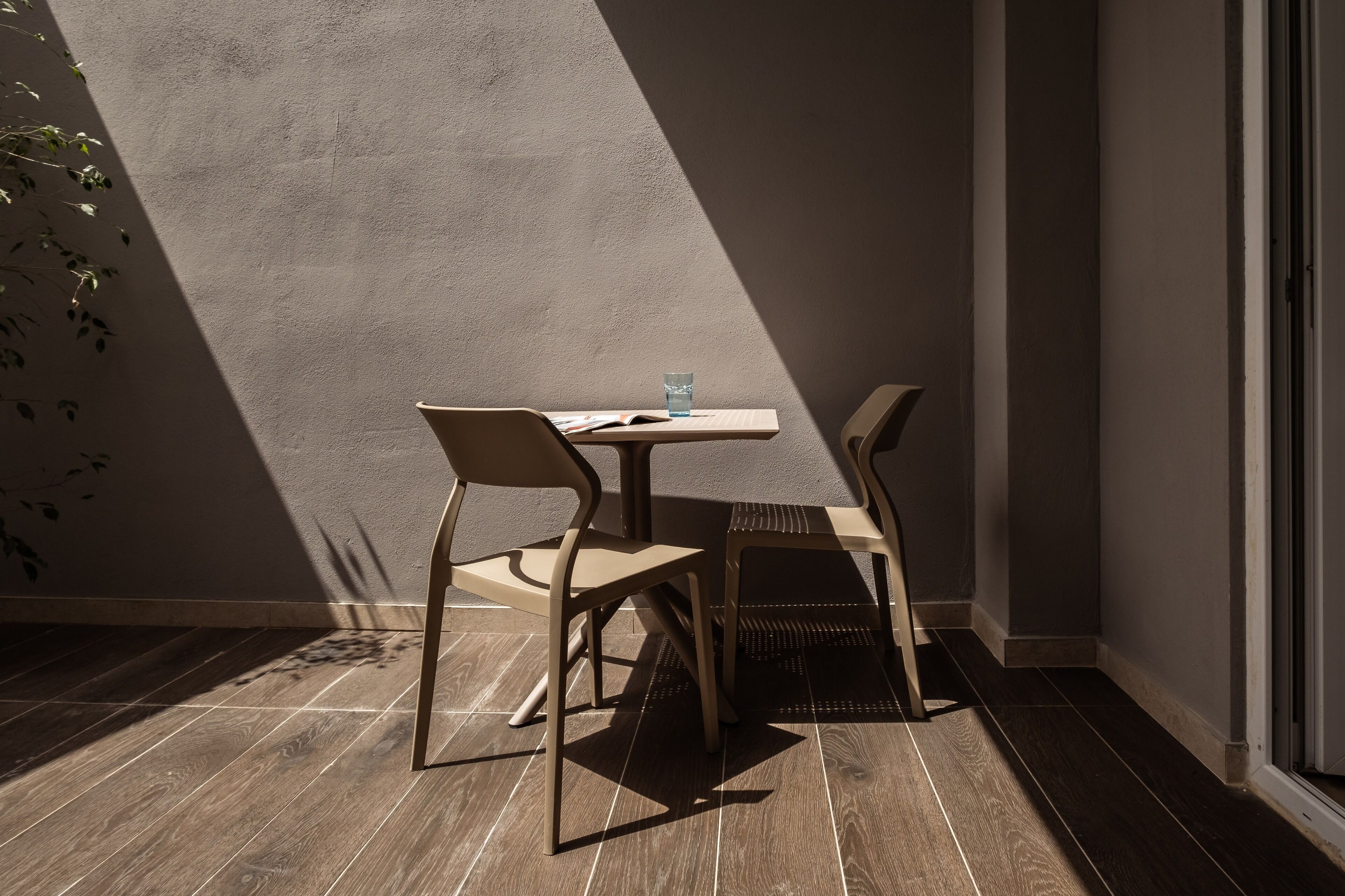 Un coin de pièce avec une table et deux chaises, un verre d’eau sur la table et une plante sur la gauche.