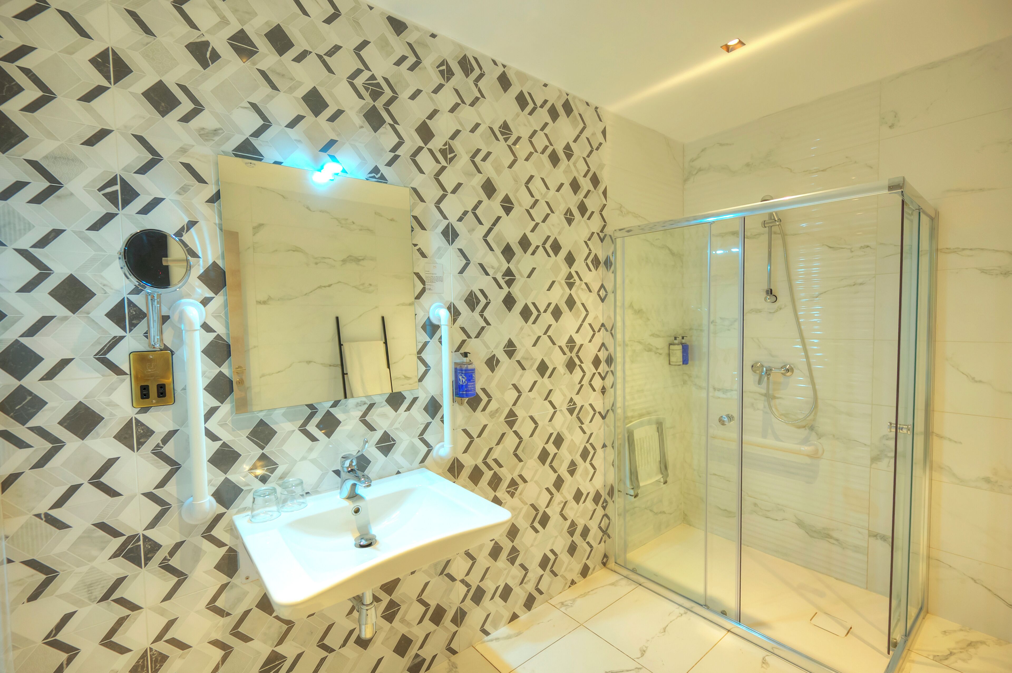 A bathroom with a geometric patterned wall, a white sink, and a glass shower enclosure.