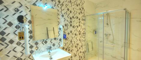 A bathroom with a geometric patterned wall, a white sink, and a glass shower enclosure.
