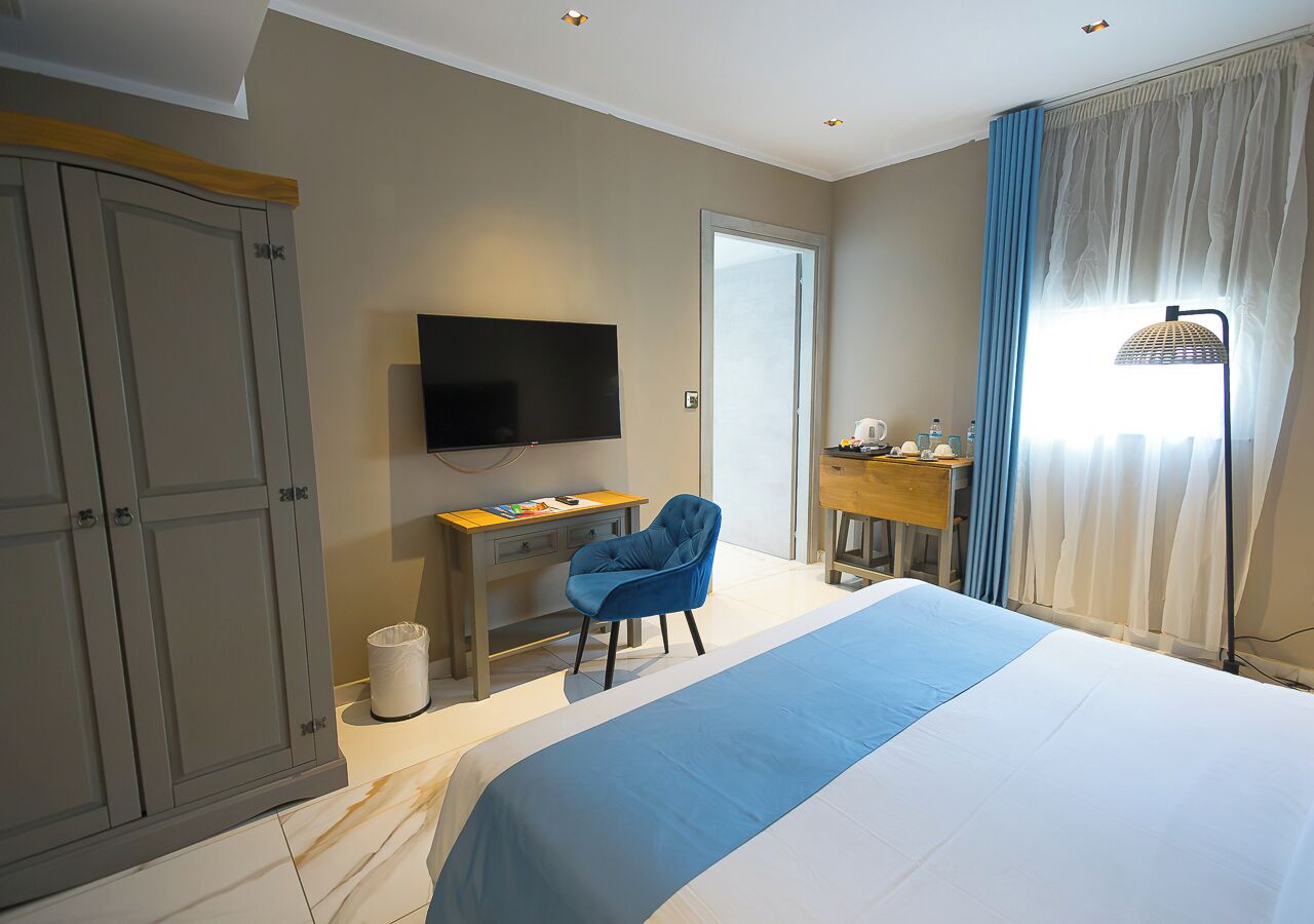 Ein Hotelzimmer mit einem großen Bett, einem Schreibtisch mit Stuhl, einem Fernseher und einem Kleiderschrank.