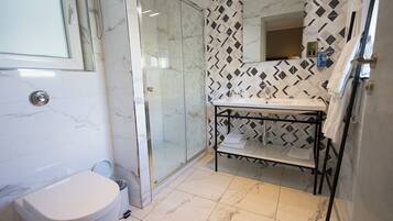 A bathroom with a toilet, a glass shower enclosure, a sink with a black metal shelf, and a patterned wall.