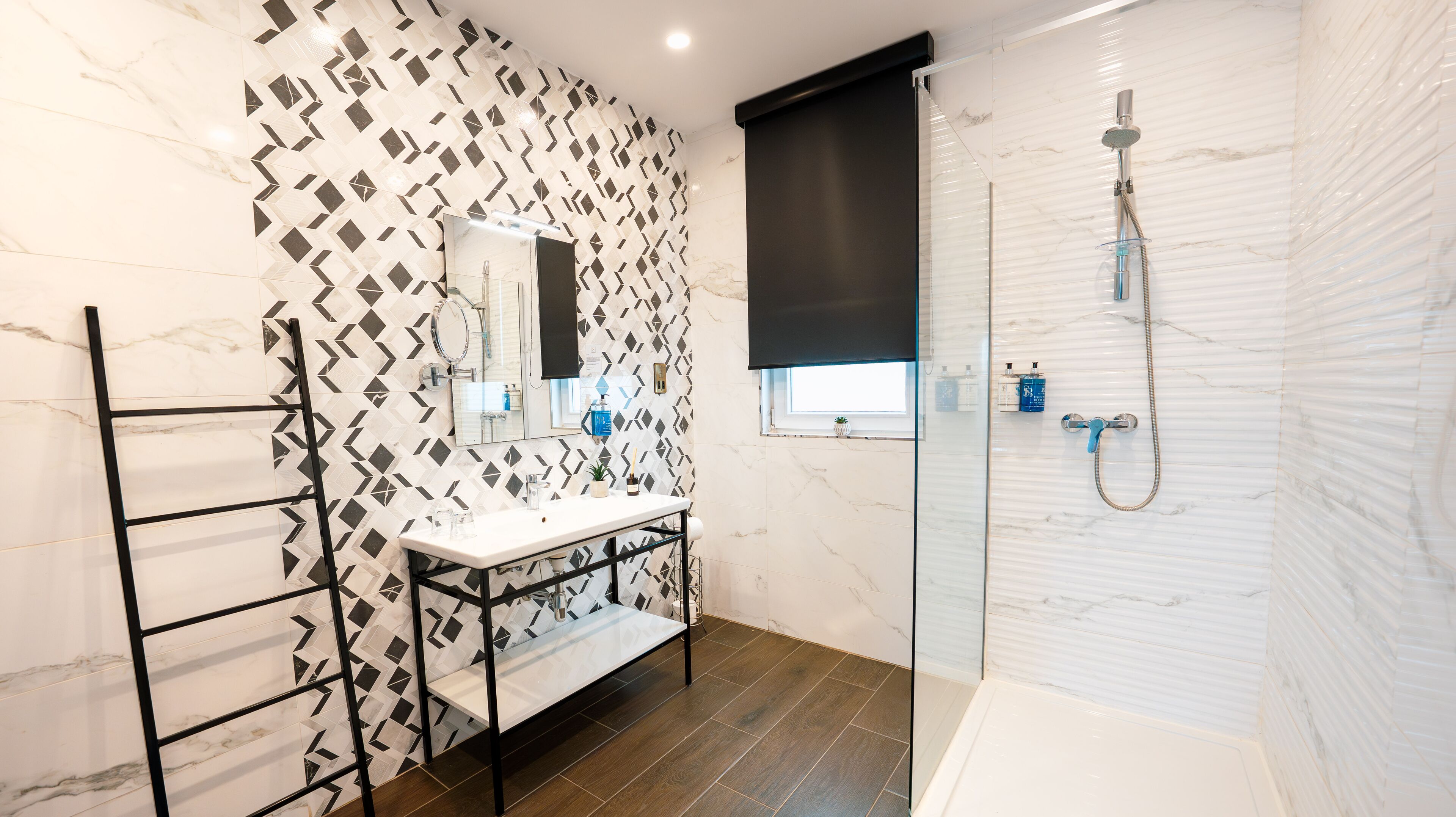 A modern bathroom with a marble vanity, a glass shower enclosure, and a wooden floor.