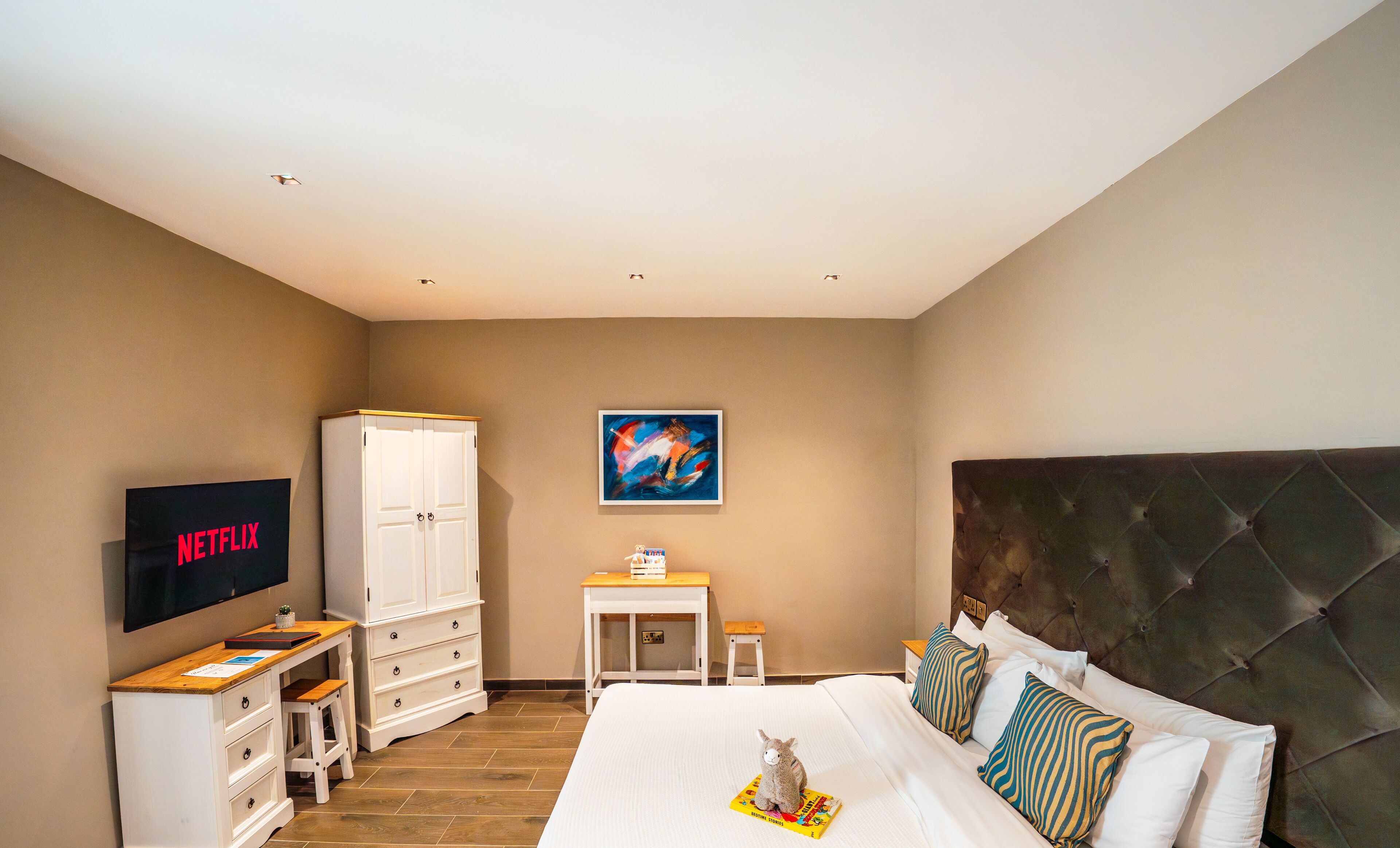 A hotel room with a bed, a TV, a wardrobe, a small table, and a painting on the wall.