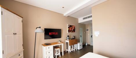 Une chambre d’hôtel comprenant un lit, un bureau avec une chaise, un téléviseur fixé au mur, une armoire et une salle de bain visible à travers une porte ouverte.