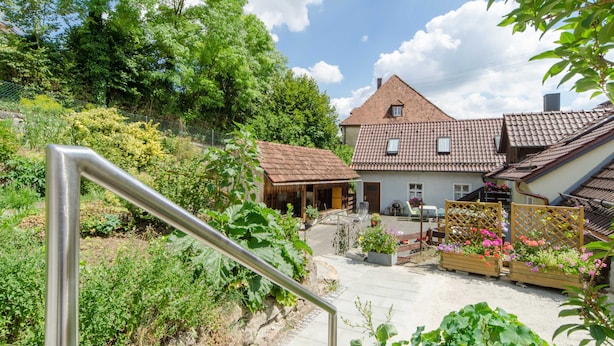 Une maison avec un toit en tuiles, un jardin avec différentes espèces de plantes et une clôture en bois.