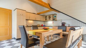 Une cuisine avec une table, des chaises et un banc en bois. Les murs sont recouverts de carreaux et le plafond est en bois.